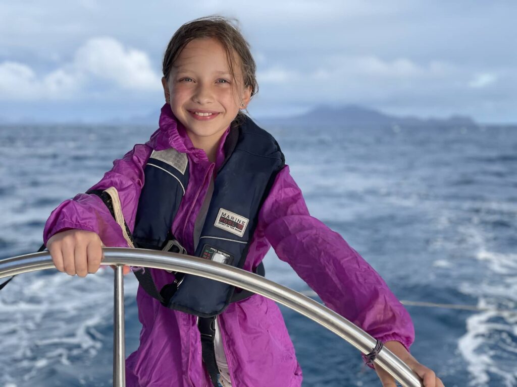 Une jeune fille à la barre du voilier, soleil couchant, retour des Saintes